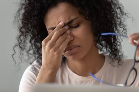 Unhappy African American woman taking off glasses close up, feeling eye strain, tired exhausted female worker, student, freelancer suffering from dry eyes syndrome, vision health problem conceptの写真素材