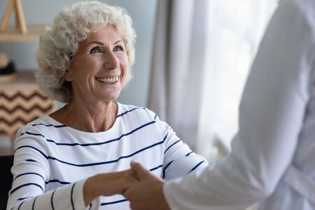 Happy grandma holding hand of nurse caregiver helping senior patient getting up taking care of...