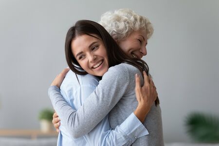 Happy young lady adult daughter granddaughter visiting embracing hugging old senior retired grandmother cuddling bonding, two age generations women expressing love and care at reunion meeting at homeの写真素材