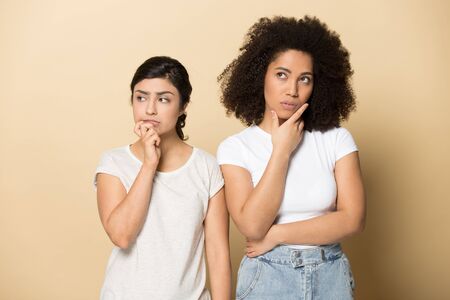 Puzzled thoughtful diverse girls touching chin with fingers, planning future, two female customers...