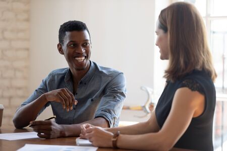 Laughing young african american male employee joking with pleasant female colleague at office. Head shot positive biracial millennial businessman having fun with businesswoman partner at meeting.の写真素材