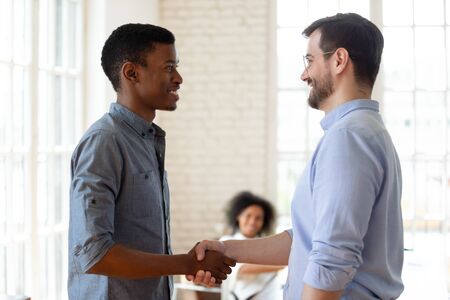 Head shot side view confident company leader in eyeglasses shaking hands with happy african american...