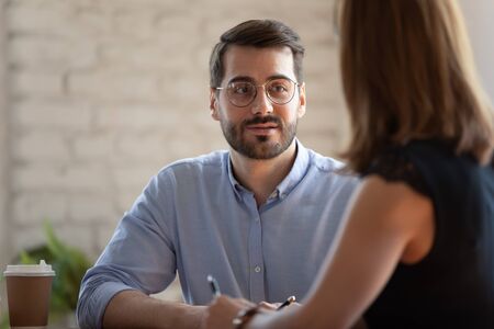 Head shot pleasant young businessman in eyeglasses holding meeting with female partner. Happy male entrepreneur listening to colleague. Friendly smiling teammates discussing project ideas at office.の写真素材