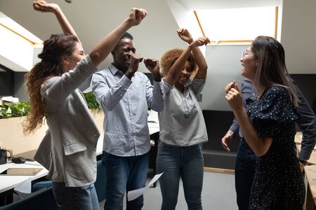 Overjoyed millennial multiracial team members enjoying party in modern coworking office. Happy mixed race young employees celebrating end of workday, dancing, having fun at workplace on friday.の写真素材