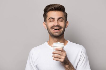 Close up head shot image of happy smiling handsome bearded man enjoying drink. Young student holding...