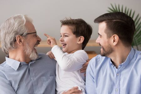 Laughing grandfather hugging little grandson, three generations of men having fun at home, happy...