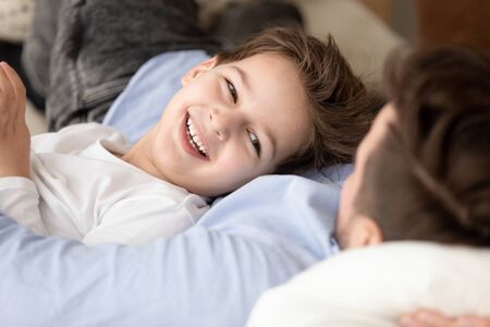 Cute little son lying on dad, cuddling and hugging preschool child relaxing with loving father, family spending weekend at home, having fun, enjoying free time, good relationship, close upの写真素材