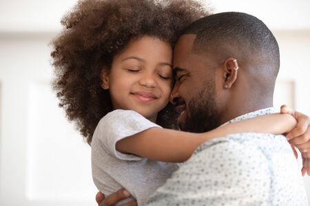 Happy african American young father hold small preschooler daughter in arms enjoying intimate close moment together, smiling biracial dad and little girl kid hug cuddle showing love and careの写真素材