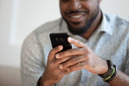 Close up of smiling african American man hold new model modern cellphone texting chatting, happy biracial male use fast connection mobile internet on cellphone browsing web. Technology conceptの写真素材