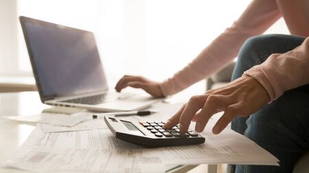 Close up of woman sit at home using laptop and calculator analyze charges calculate monthly home...