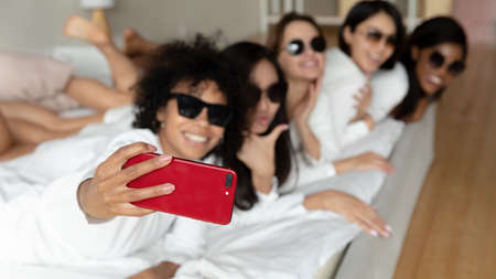 Happy young pretty multiethnic women best friends wear sunglasses and bathrobes take selfie on...