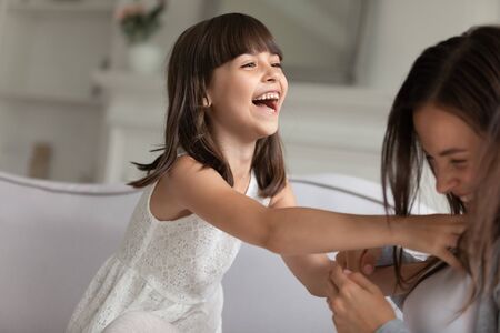 Focus on little laughing daughter enjoy funny game playing with young mother, different age sisters having fun at home. Warm relations between multi generational relatives, playtime activities conceptの写真素材