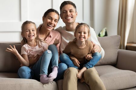 Happy family of four young parents and cute small funny children daughters bonding sit on sofa...