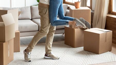 Young couple first time home owners celebrate moving day concept, man husband lifting holding wife...