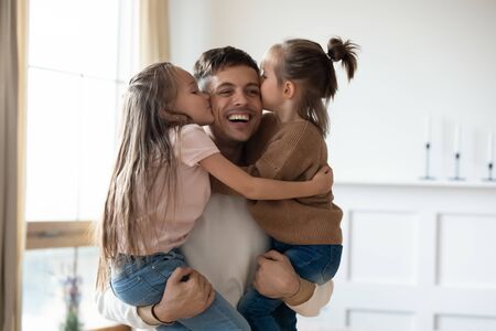 Funny cute small daughters kiss happy daddy on cheeks congratulate with fathers day, cheerful dad...