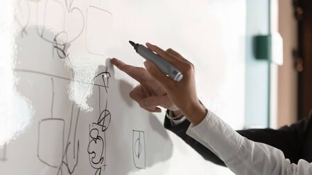 Crop close up of diverse businesspeople write on white board in office brainstorm discussing company strategies, colleague or employees draw graph consider plan or project in boardroom togetherの写真素材