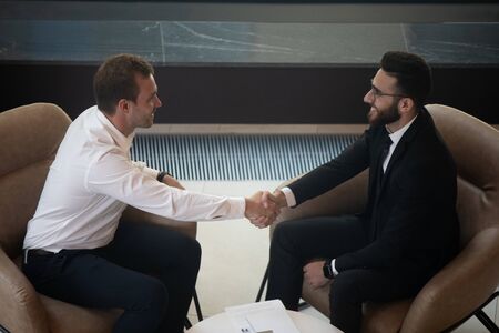 Top view of smiling multiethnic businessmen shake hand greeting or getting acquainted at briefing, happy international male business partners handshake closing deal sign contract at negotiationsの写真素材