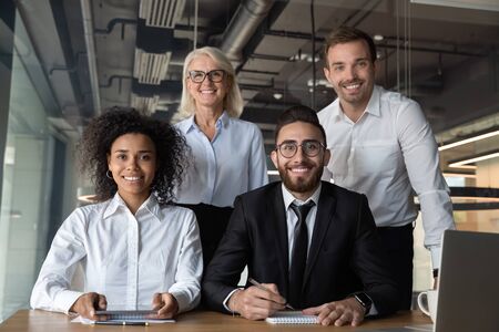 Portrait of smiling multiracial businesspeople marketing department posing at desk in modern office,...