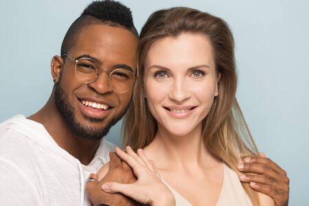 Head shot smiling African American man and beautiful Caucasian woman posing together, embracing shoulders, looking at camera, natural beauty concept, standing isolated on studio background close upの写真素材