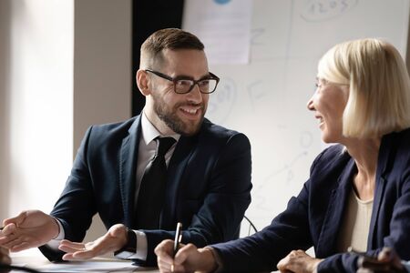 Head shot smiling businessman in eyeglasses talking to pleasant middle aged female partner. Happy male executive boss leader discussing project details, communicating with positive older employee.の写真素材