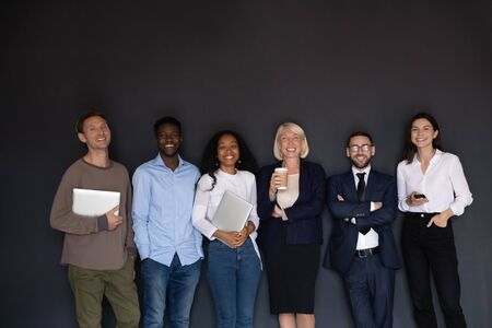 Portrait of happy mixed race older and young employees standing in row line, isolated on black studio background. Smiling multiracial group of expert professional company staff looking at camera.の写真素材