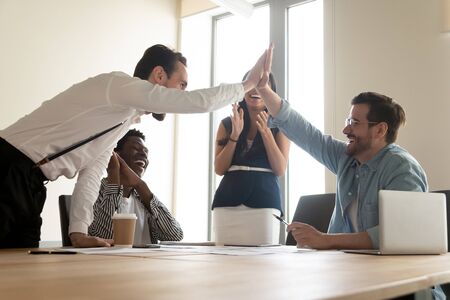 Happy multiracial department celebrating successful project accomplishment, guys team leaders giving high five feels excited, unity, sharing common success, reward and promotion career growth conceptの素材 [FY310134588052]