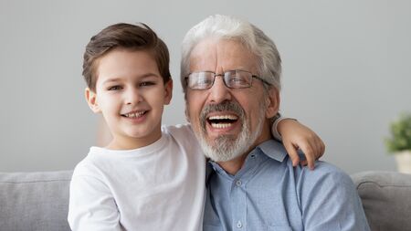Head shot portrait little grandson embraces grey-haired elderly grandfather family spend time together sit on couch at homeの写真素材
