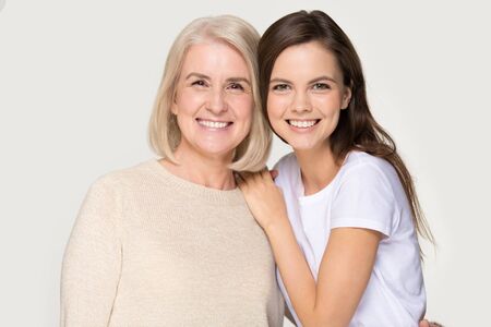 Laughing caring granddaughter embrace grandmother. Studio headshot isolated on grey background.
