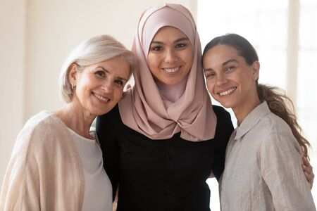 Head shot close up portrait muslim businesswoman in hijab embracing happy middle aged and young mixed race colleagues. Multiracial diverse female coworkers international team posing for photo.の写真素材