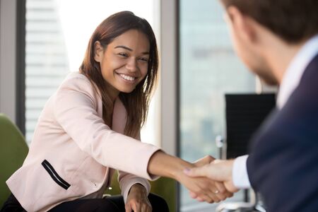 Smiling African American businesswoman shaking hand of businessman, business partners, candidate and...