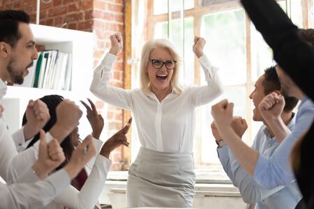 Excited happy diverse staff in spotlight overjoyed middle-aged woman team leader screaming with joy, department celebrating business success make great deal, fantastic results, growth of sales conceptの写真素材