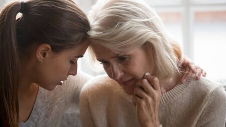 Close up of loving millennial adult daughter and elderly crying mom feel sad depressed share family loss grief together, supportive grownup female hug comfort unhappy senior mother show love and careの写真素材