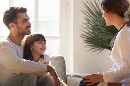 Friendly pediatrician doctor consulting father about little daughter health, smiling dad hugging child at doctor office, patient listening to therapist consultation, children medical insurance careの写真素材
