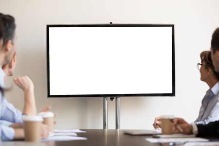 Focused business people gather at boardroom sitting at desk looking at tv white mock up with copyspace blank screen for advertisement. Seminar, presentation, corporate team at company training conceptの写真素材