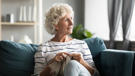 70s old woman sit on sofa, distracted from hand knitting grandmother look out window enjoy scenery at sunny weather reduces stress, take break without feeling useless, hobby free time activity conceptの写真素材
