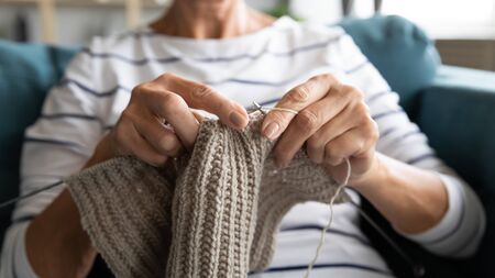 Close up view grandmother hands holding needles make repetitive motion knitting sitting on couch...