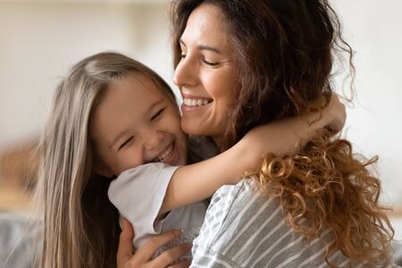 Close up beautiful young mother snuggle little cheerful daughter laughing enjoy moment of tenderness having fun spend time together at home, next generation and offspring, unconditional love conceptの写真素材