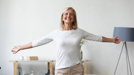 Overjoyed middle-aged grandmother female pensioner stretch hands have fun dance in living room at homeの写真素材