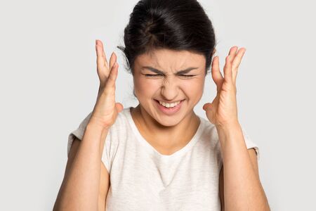 Irritated stressed millennial indian woman cant stand noise, feeling crazy mad isolated on grey...
