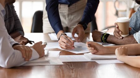 Close up of multiethnic millennial colleagues coworkers sit at office desk discuss business ideas consider paperwork together, diverse businesspeople brainstorm over financial statistics at meetingの写真素材