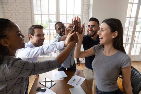 Top view of happy multiethnic young employees join hands give high five celebrating business success at meeting, excited diverse colleagues coworkers involved in teambuilding activity show team spiritの写真素材