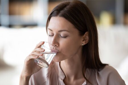 Beautiful young woman drink clean still mineral water from glass for body refreshment, thirsty...
