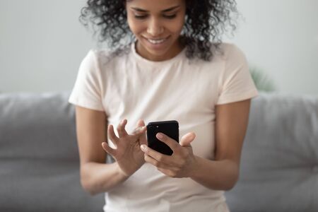 African woman sitting on couch holds smartphone close up focus on hands and gadget, 30s active media social networks user download new free application, chatting online, using e-dating service conceptの写真素材