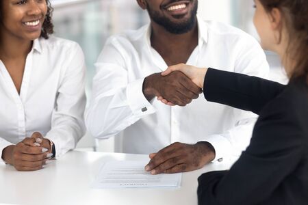 Close up of happy black couple handshake female real estate agent closing cooperation deal in office, excited african American husband and wife shake hand of woman broker make agreement buying houseの写真素材