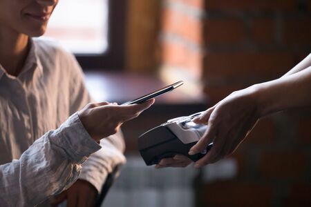 Close up of female restaurant or cafe client paying for order using cellphone with nfc technology,...