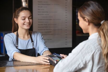 Smiling waitress give terminal for client to make payment using credit card and modern contactless...