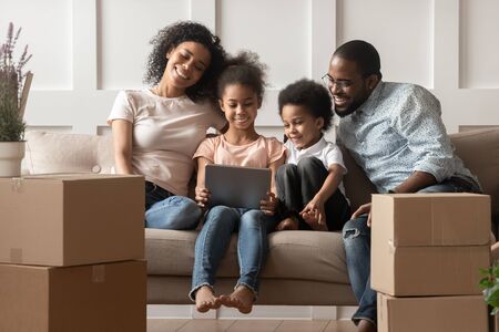 Happy smiling african american family of four sitting together on couch in modern living room, cute...