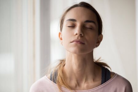Close up calm mixed race millennial woman in casual clothes sitting with closed eyes, relaxing, meditating, doing breathing exercises, thinking, reminding good memories, visualizing future.の写真素材