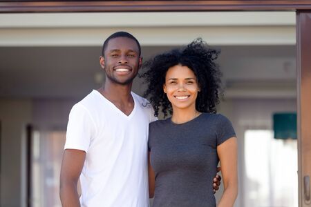 Portrait of happy young African American family stand outside own home, smiling black husband and wife posing outdoor new country house together, first time buyers excited with property purchaseの写真素材