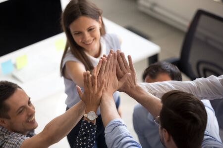 Close up of smiling young office colleagues give high five motivated for shared goal or success,...